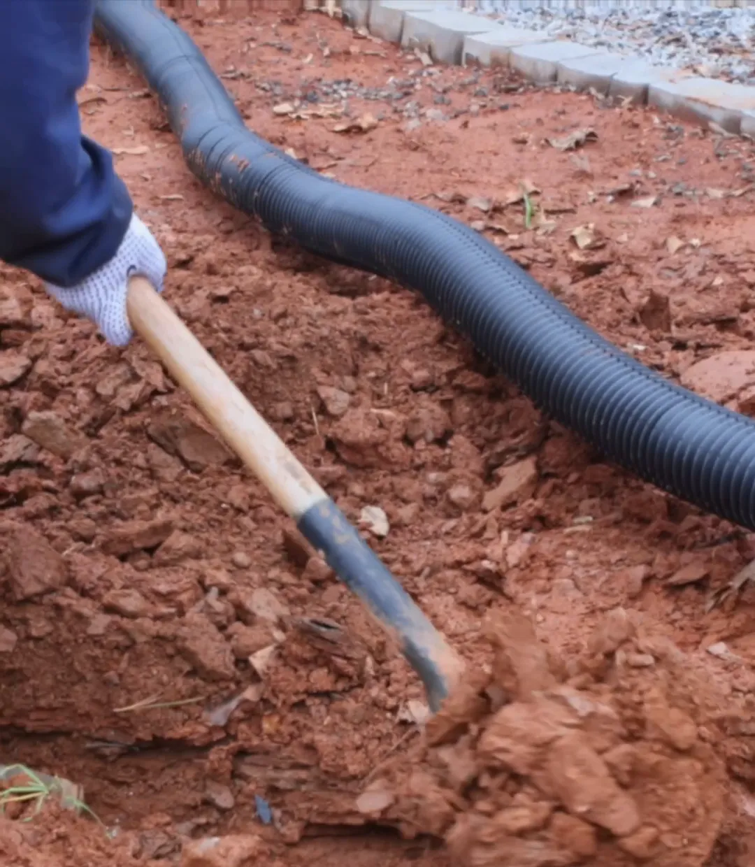A worker shovelling soil beside a newly laid drainage pipe