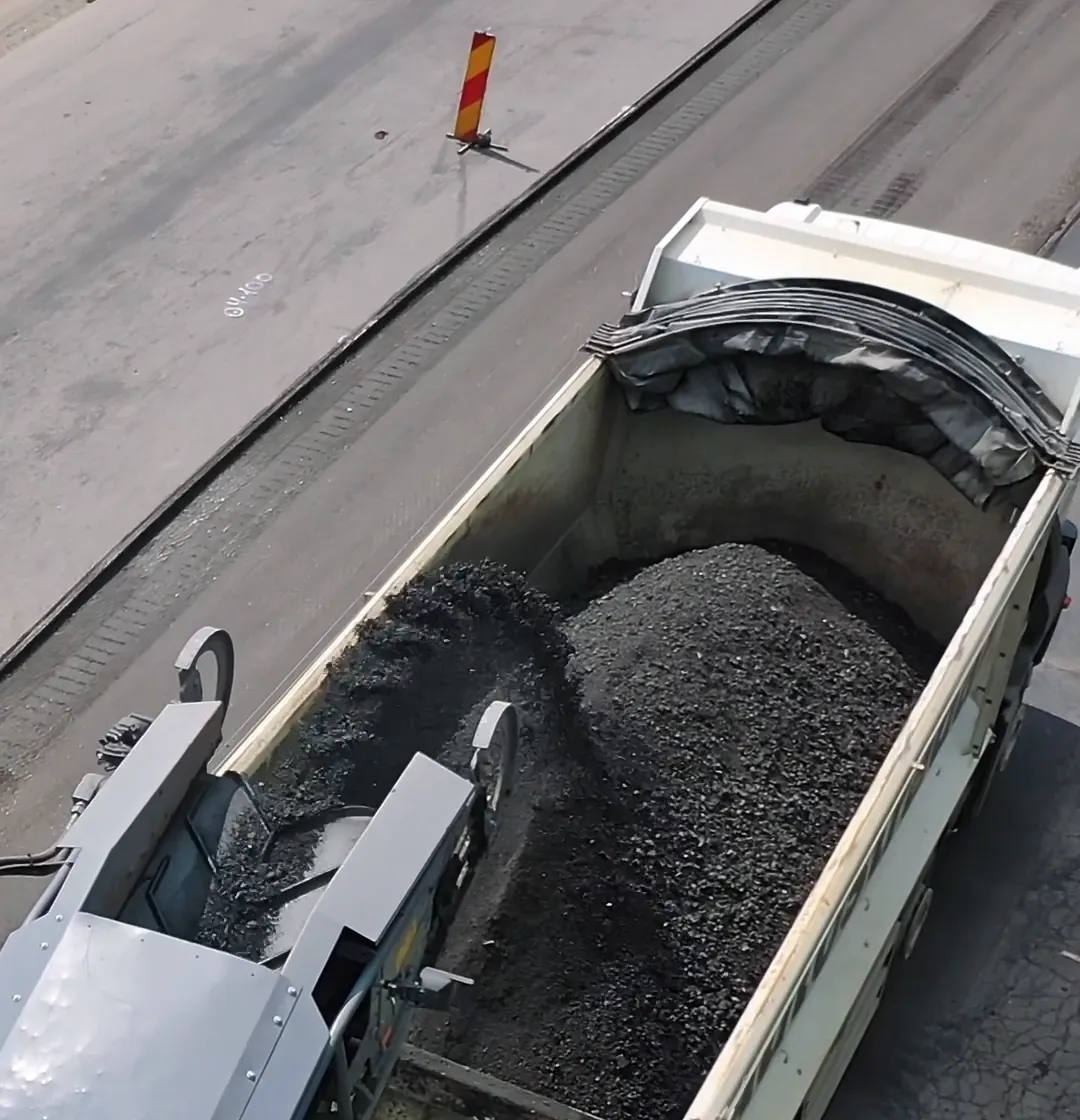 A road crew milling a residential street, loading old asphalt into a dump truck